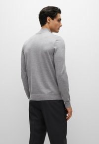 Maglione grigio a maglia con colletto tondo, polsini e orlo a coste. Texture morbida, design aderente e dettagli di cucitura discreti sulle spalle.