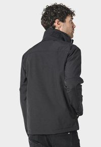 Czarna kurtka softshell z wysokim kołnierzem, z przeszyciami i logo na szyi. Regulowane mankiety i dopasowany krój.