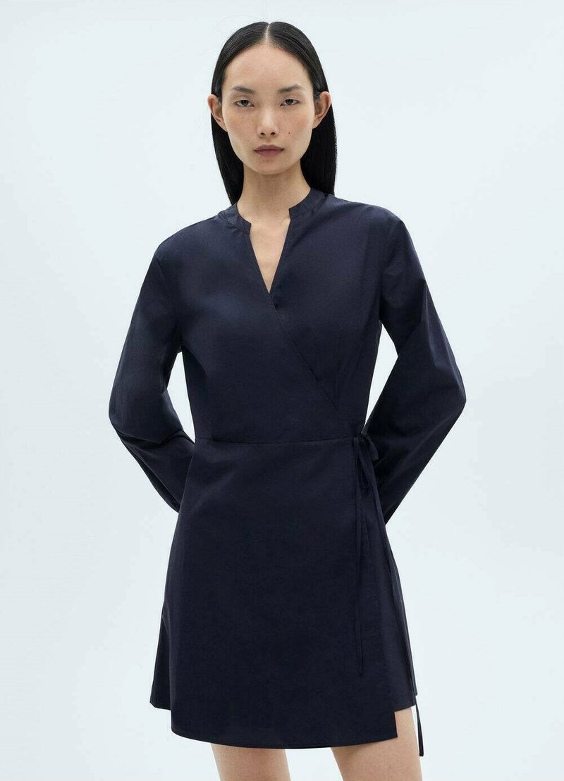 Rochie în nuanță de bleumarin, cu mâneci lungi, decolteu în V, talie legată și un tiv ușor evazat. Fabrică netedă și design minimalist.