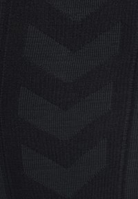 Gros plan sur un tissu noir avec un motif texturé de trois chevrons pointant vers le bas dans une teinte légèrement plus claire.