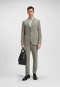 Jasnoszary garnitur z dwiema kieszeniami, dopasowany krój, teksturowany materiał. Czerwona skórzana torba w ręku, wypolerowane czarne buty, wzorzysty shirt pod spodem.