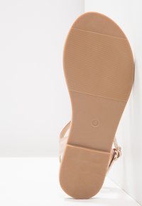 Nude sandaalit, joissa on sileä, nahkamainen päällinen ja teksturoitu kumipohja. Varustettu säädettävällä soljella ja minimalistisella muotoilulla.