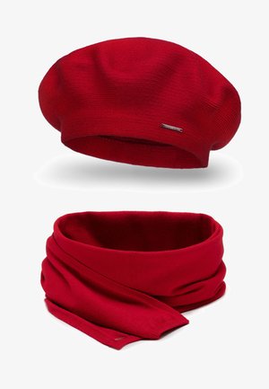 Berretto lavorato a maglia rosso con una texture liscia e un piccolo logo metallico. Sciarpa lavorata a maglia rossa abbinata, caratterizzata da un design morbido e senza cuciture.