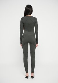 Body aderente verde scuro e leggings con motivi texturizzati e dettagli di cucitura, maniche lunghe e vita alta.