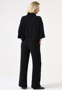 Schwarzes, strukturiertes Outfit mit einer lässigen Bluse mit Stehkragen und weiten Hosen, beide mit einer weichen, gerippten Oberfläche.