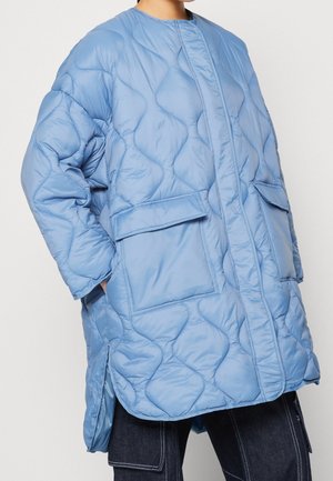 Chaqueta acolchada de color azul claro con cuello redondo, que cuenta con dos bolsillos frontales con solapa. La tela tiene una textura suave y brillante.