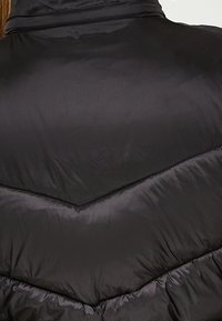 Chaleco de plumas negro con un patrón en forma de chevron, con una textura suave y brillante, cuello alto y costura acolchada.