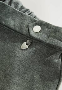 Sivá textília s hladkou štruktúrou a volánovým opaskom. Obsahuje strieborný gombík a srdiečkový prívesok s gravírovaním "Clarks".