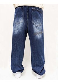 Pantalones vaqueros de denim oscuro de corte holgado con parches desgastados, diseño de cinco bolsillos y bordado en el bolsillo trasero izquierdo.
