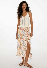 Světlý pletený krémový top bez rukávů s texturovaným vzorem, spárovaný s sukní po kolena s květinovým potiskem, na které jsou kaktusy v oranžové, šedé a růžové barvě.