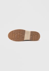 Sko sål med et mønster af spor i brunt gummi, med en central tan sektion med et brandlogo og tekstureret greb for traction.