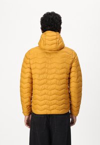 Giacca puffer gialla con cappuccio, caratterizzata da un motivo a zig-zag. Il materiale sembra leggero e liscio al tatto.