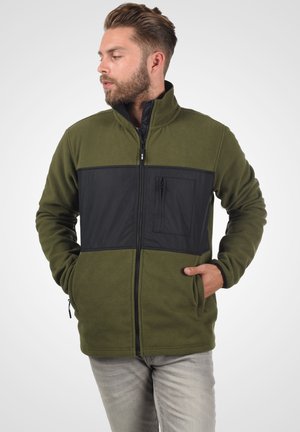Fleece jacket in olive green with black paneling, zippered front, high collar, and chest pocket. Features two side pockets.