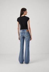 Svart skjorte med korte ermer, kombinert med lyseblå flared jeans. Jeansen har en falmet finish og to baklommer, med en synlig etikett.