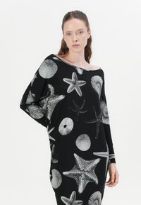 Schwarzes, übergroßes Kleidungsstück mit langen Ärmeln, das mit weißen Seestern- und Muschelmustern verziert ist. Es zeigt ein entspanntes Design und eine weiche Textur.