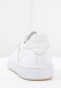 Vit lädersneaker med en texturerad bakhälla, som har en mjuk krage och en gummisula. Minimalistisk design med subtila detaljer.