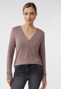 Helles Mauve-Oberteil mit langen Ärmeln, V-Ausschnitt und weicher Textur, kombiniert mit dunkelgrauen Jeans. Einfaches Design ohne Muster oder Akzente.