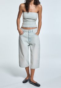 Top senza spalline azzurro chiaro abbinato a culotte ampie in denim chiaro, dotate di tasche frontali e una vestibilità rilassata. Scarpe basse nere con borchie.
