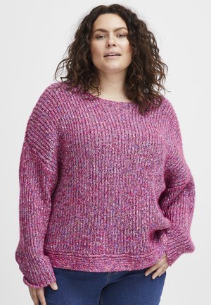 Chunky rosa stickad tröja med vid halsringning, ribbad textur och sänkta axlar, med flerfärgade fläckar genom hela plagget.