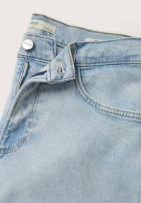 Jeans de mezclilla azul claro con cremallera y cierre de botón. Presentan costuras decorativas y un acabado limpio alrededor de los bolsillos y la pretina.