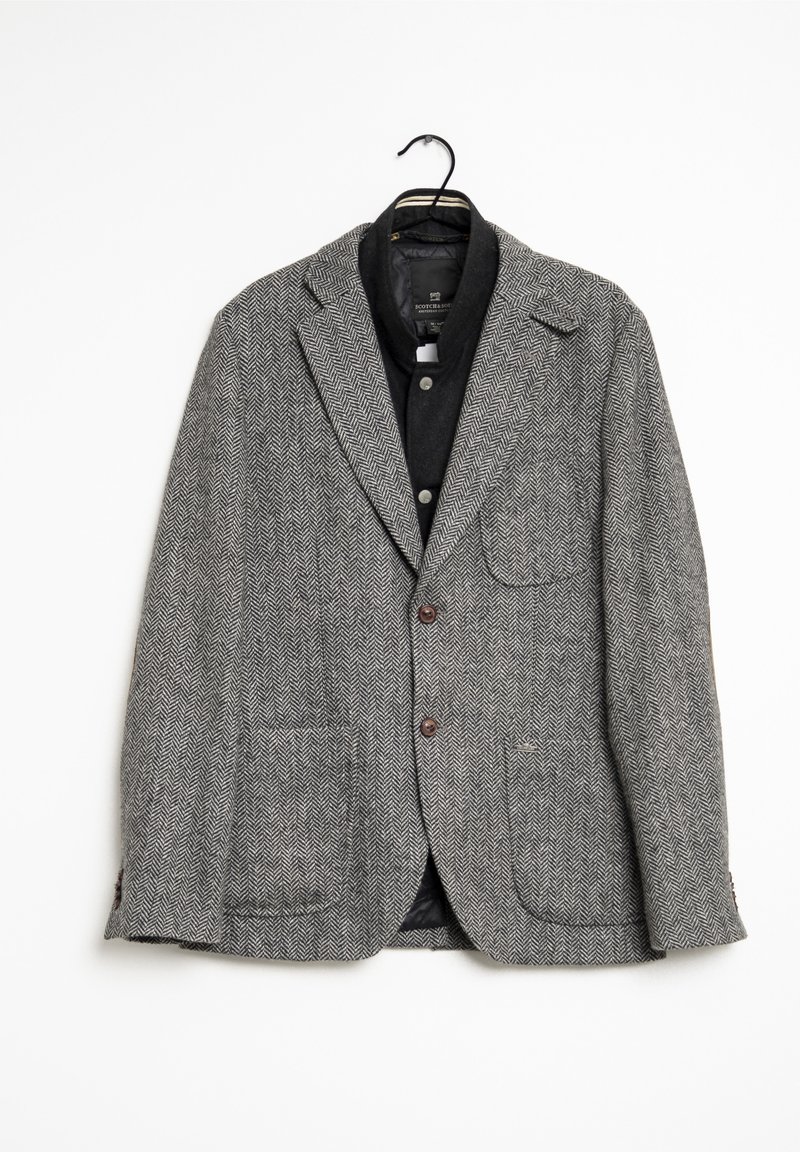 Grå herringbone-blazer gjord av strukturerad tyg, med två framfickor, bruna knappar och slagkrage. Hänger från en svart krok.