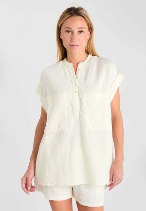 White, textured short-sleeve tunic with a mandarin collar and three buttons, featuring two front pockets. Paired with matching shorts.