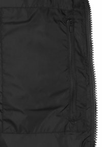 Interno di una giacca a vento nera con una tasca con zip in tessuto texturizzato. Il materiale appare liscio e leggero, caratterizzato da un colore uniforme.