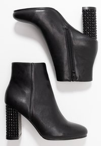 Para czarnych skórzanych botków sięgających kostki z dekoracyjnymi, ćwiekowanymi obcasami oraz zamkami błyskawicznymi po bokach na białym tle.