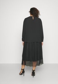 Top nero a maniche lunghe con dettaglio a occhiello sul retro, abbinato a una gonna nera plissettata e tacchi a stiletto neri.