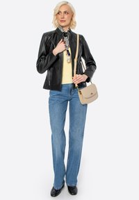 Giubbotto di pelle nera con chiusura a zip, top giallo, jeans a gamba larga blu e una borsa leggera color beige. Gli accessori includono una sciarpa stampata.