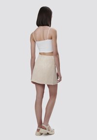 Top bianco corto con spalline sottili abbinato a una mini gonna texturizzata di un leggero beige e sandali chunky beige. Design liscio e aderente.