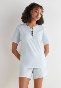 Lichtblauw gestreept pyjama-set met een T-shirt met korte mouwen en een vetersluiting aan de halslijn, en bijpassende shorts met een elastisch tailleband. Zachte stof.