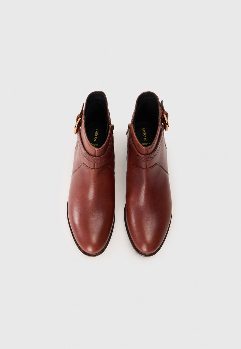 Stivali alla caviglia in pelle marrone con punta appuntita, parte superiore texturizzata, dettaglio fibbia laterale e finitura liscia. Presentano una soletta imbottita.