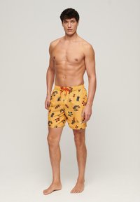 Boxer da nuoto giallo con stampa floreale e tropicale, dotato di cintura con cordino e realizzato in un tessuto leggero e non restrittivo.