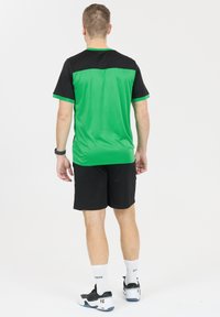 Urheiluasu, joka koostuu vihreästä ja mustasta lyhythihaisesta paidasta, mustista shortseista ja mustista urheilukengistä, joissa on valkoisia yksityiskohtia.