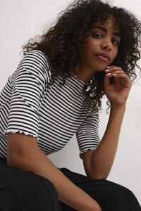 Gestreepte, geribbelde top in wit en marineblauw met een hoge hals en korte mouwen met gegolfde randen, gedragen met zwarte onderkleding.