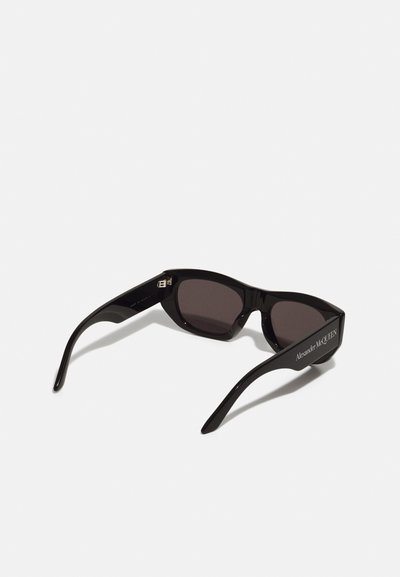 Occhiali da sole neri con un design elegante e angolare, lenti scure e dettagli del logo sulle aste. Realizzati in materiale plastico lucido.