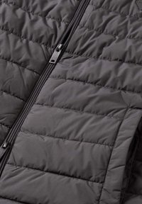 Gewatteerd zwart vest met rits, horizontaal doorgestikt patroon en glanzende ritssluiting. Heeft een gladde stoftextuur en strakke randen.