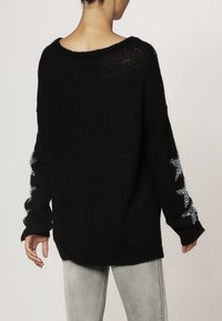 Pull noir surdimensionné en tricot doux, équipé d'un col large et d'ornements en étoile argentée sur les manches.