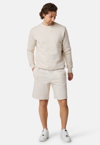 Beige sweatshirt and matching shorts made of soft, textured fabric. The outfit features a crew neckline and side pockets, paired with white sneakers.