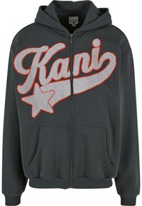 Sweat à capuche gris foncé zippé avec poches avant, présentant un grand texte en relief "Kani" et un motif étoile délimité en orange sur la poitrine.