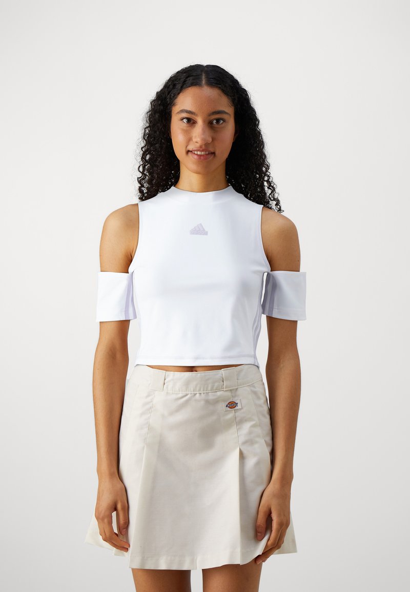Λευκό cropped top με τιράντες off-shoulder και μωβ λογότυπο adidas, συνδυασμένο με μια μπεζ φούστα που έχει επίπεδο μπροστινό μέρος και πιέτες.