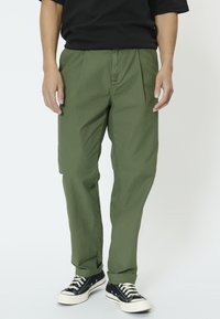 Pantalones verde oliva de corte recto y con pinzas, hechos de tela ligera, combinados con zapatillas negras de caña alta.
