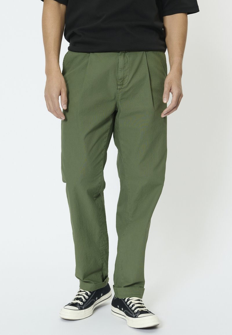 Pantalones verde oliva de corte recto y con pinzas, hechos de tela ligera, combinados con zapatillas negras de caña alta.