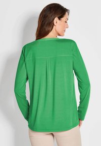 Grüne Langarmbluse aus glattem, leichtem Stoff, mit einem schlichten Design, Rückenschlitz und abgerundetem Saum.