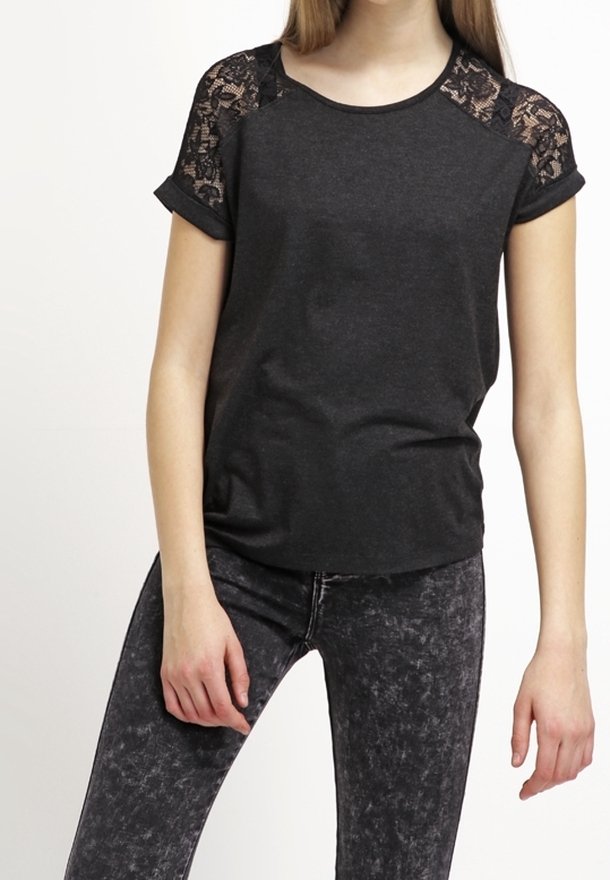 Jeune personne portant un haut noir à manches courtes avec des empiècements en dentelle aux épaules et un jean skinny noir délavé à l'acide, debout avec les bras relâchés.