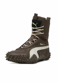 Bota marrón impermeable con una superficie texturizada, acentos en blanco y suela con pinchos. Cuenta con cierre de cordones y un cuello acolchado para mayor soporte.