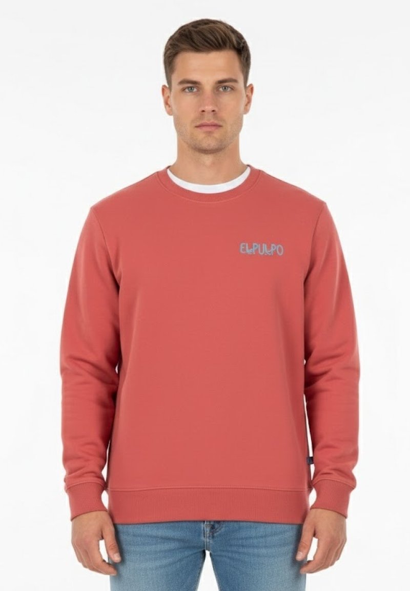 Hombre vestido con un sudadera color salmón que lleva el texto "ELPULPO" en el pecho, combinada con jeans de color azul claro, de pie frente a un fondo blanco.