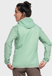 Hellgrüne Kapuzenjacke mit glatter Textur, elastischen Bündchen und kontrastierenden Verzierungen, entworfen für Komfort und Beweglichkeit.