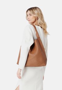 Sac en toile en cuir tressé marron avec un design décontracté et une seule bandoulière. Surface texturée et intérieur spacieux visibles.